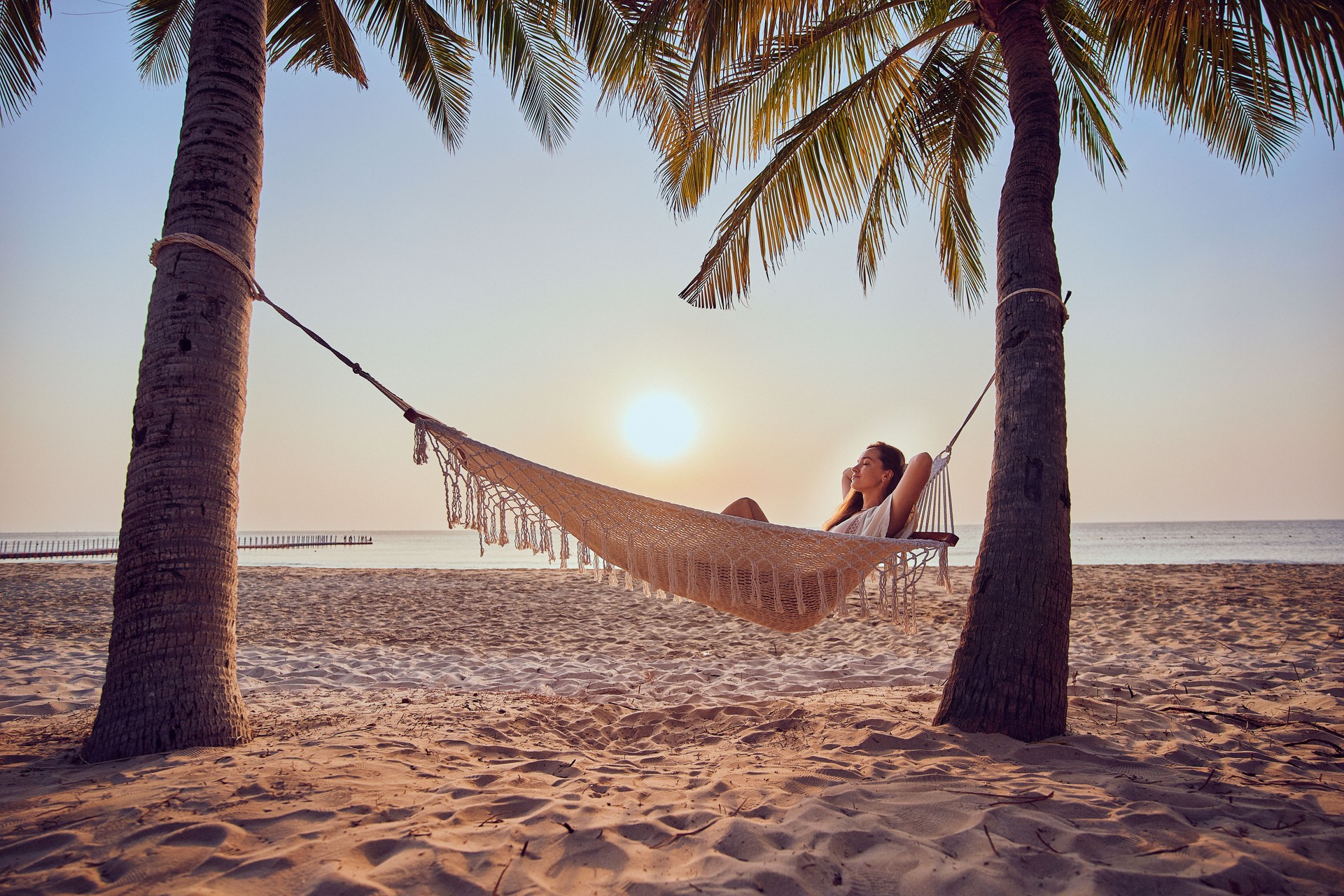 Calm woman with closed eyes and hands behind head chilling on a hammock on a tropical island among palm trees enjoying relaxing and a idyllic beautiful moment of life